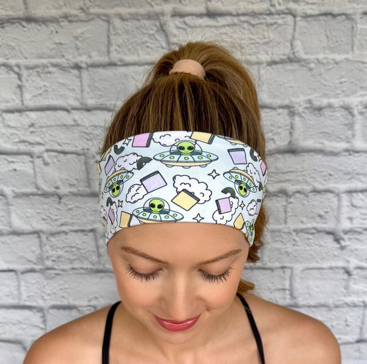 Woman with hair in ponytail wearing flat, stretchy, light blue headband with alien and space theme print.