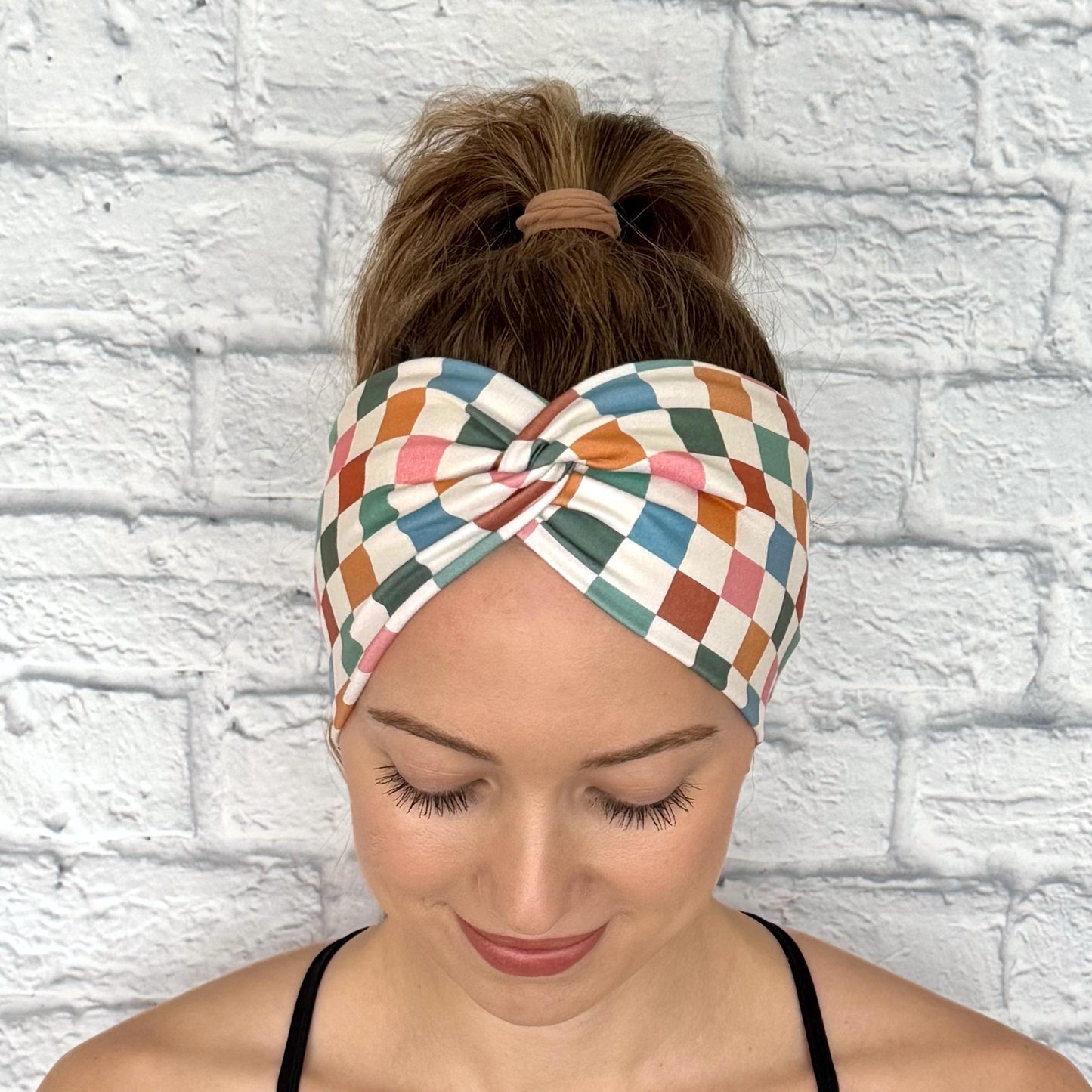 Woman with hair in ponytail wearing wide, stretchy headband in multicolor checker print.