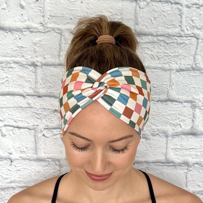 Woman with hair in ponytail wearing wide, stretchy headband in multicolor checker print.