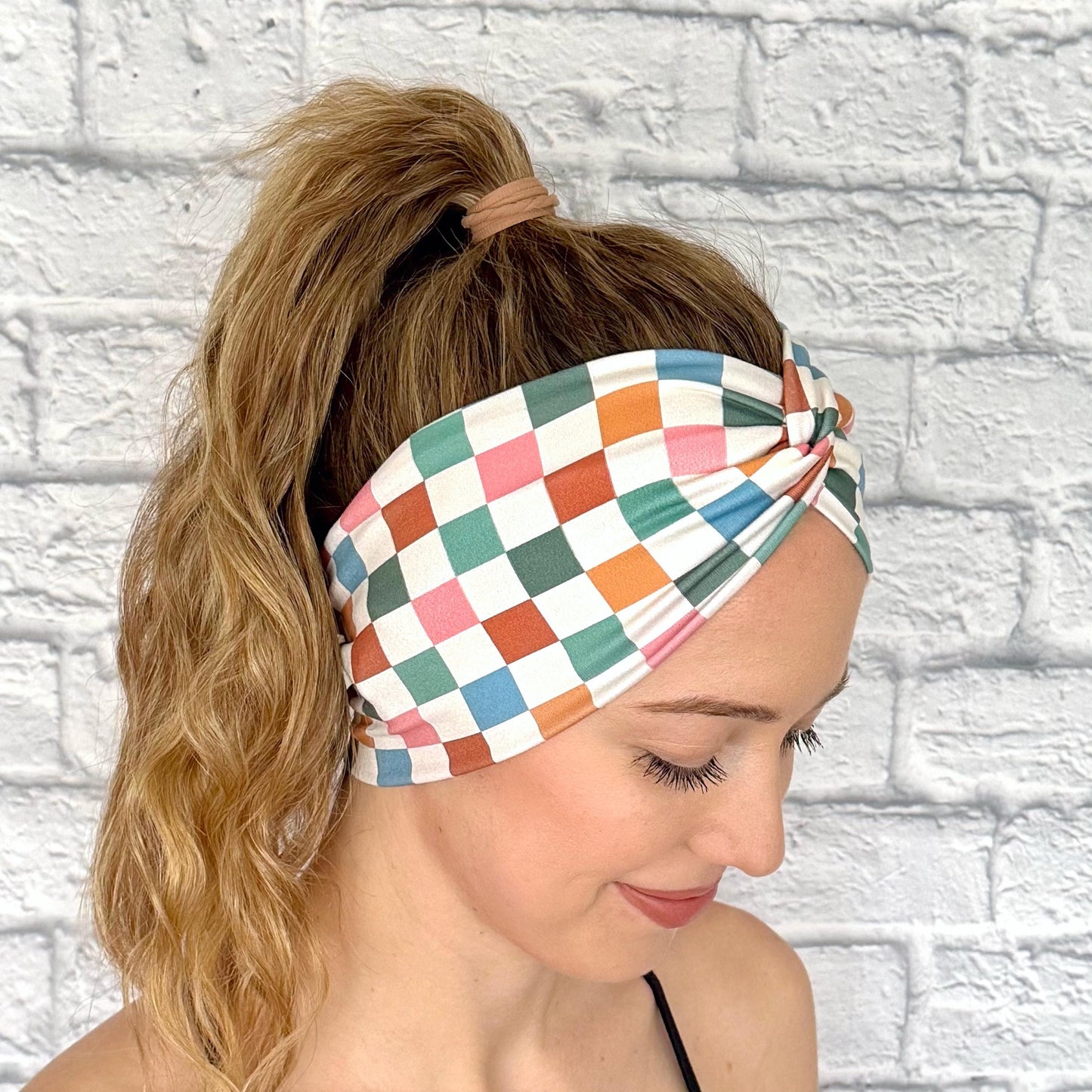 Woman with hair in ponytail wearing wide, stretchy headband in multicolor checker print.