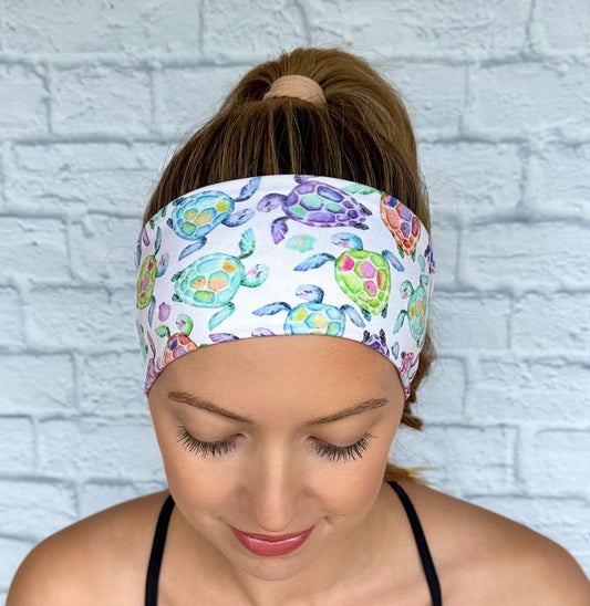 Woman with hair in ponytail wearing a flat, stretchy, white headband with sea turtle print.