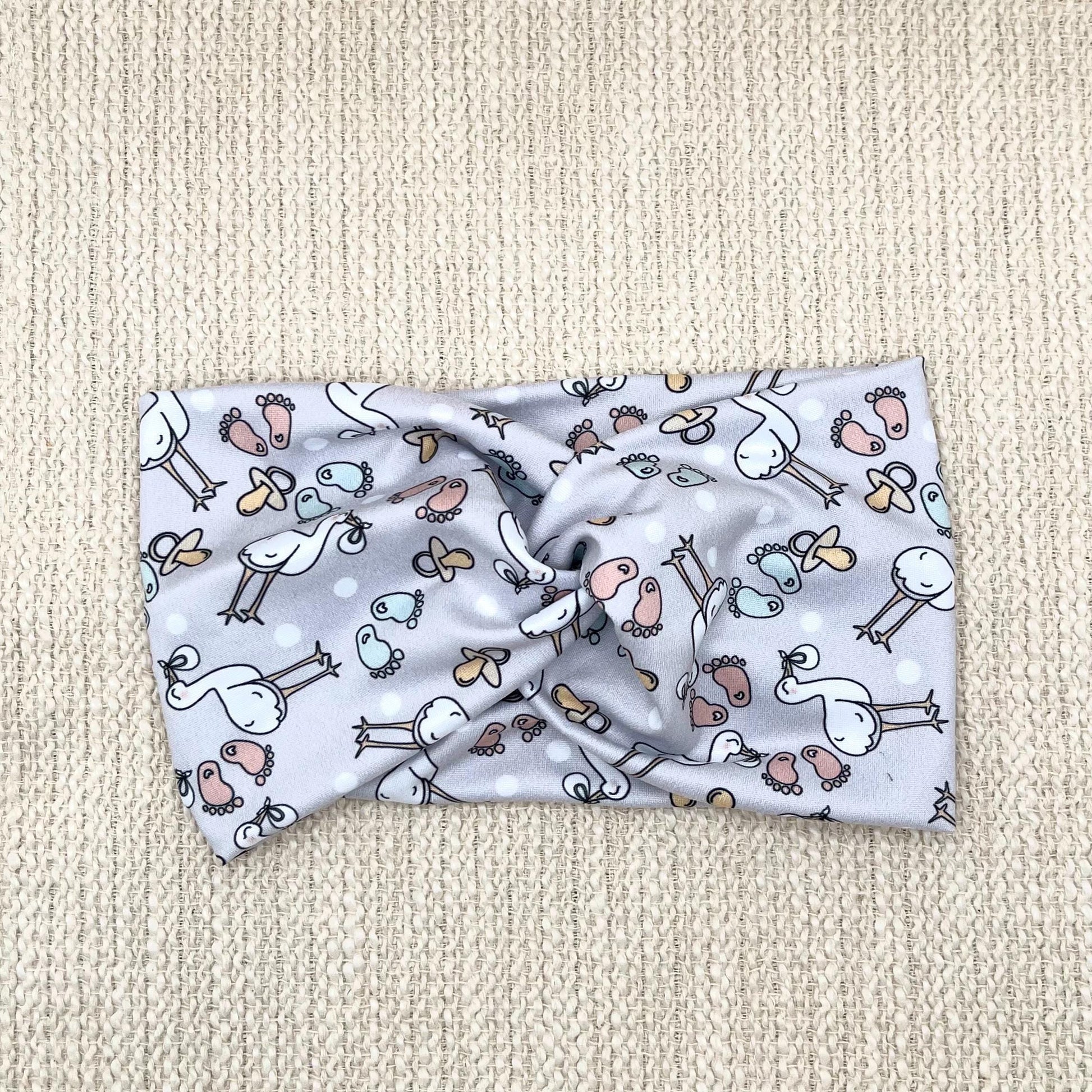 Wide, twisted, light gray headband with stork and baby theme print.