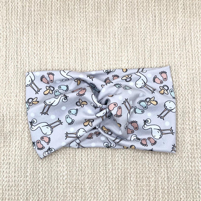 Wide, twisted, light gray headband with stork and baby theme print.