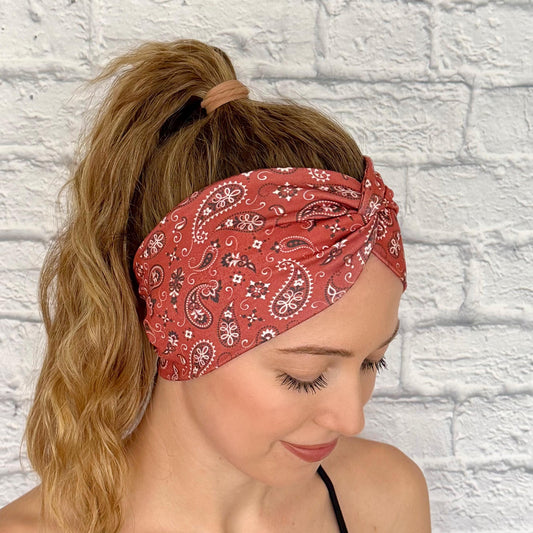 Woman with hair in ponytail wearing wide, twisted, red bandana print headband.