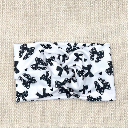 Wide, twisted, white headband with black bow print.