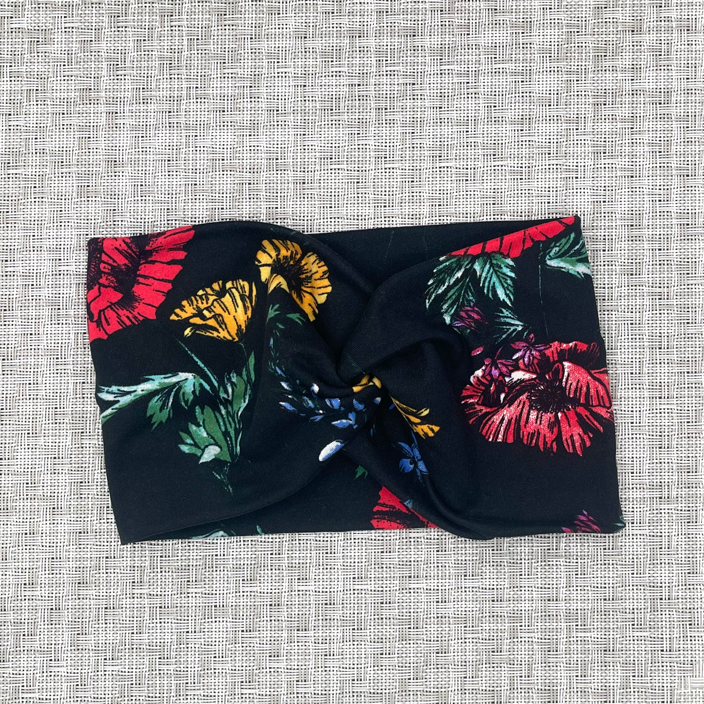 Wide, twisted, black headband with red, yellow, blue, and green floral print.