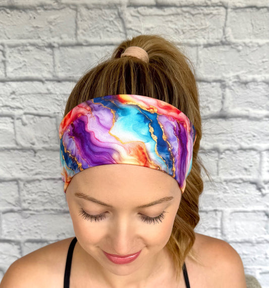 Woman with hair in curled ponytail wearing flat, stretchy headband in multi-color watercolor print.