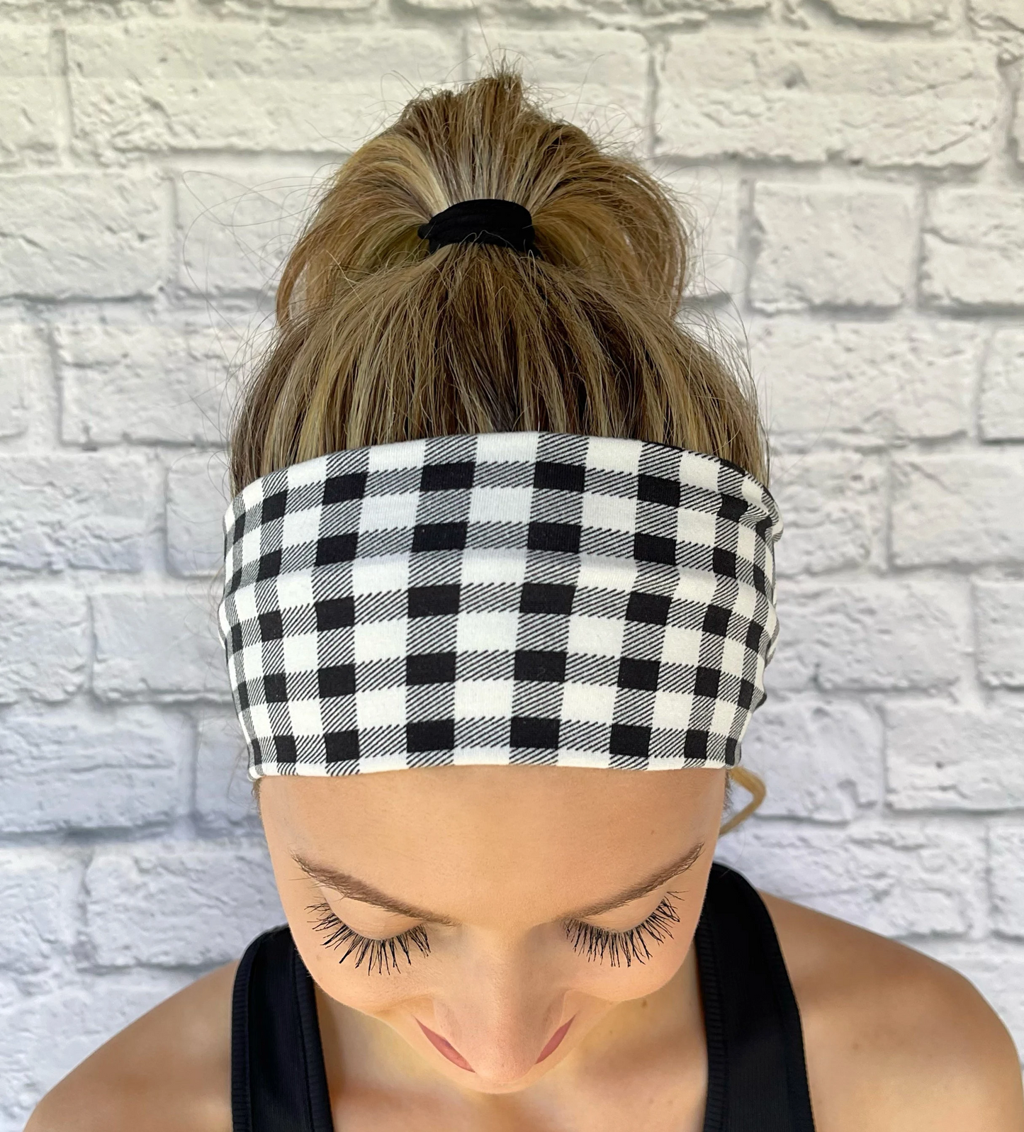 Woman with hair in ponytail wearing black and white buffalo plaid headband.