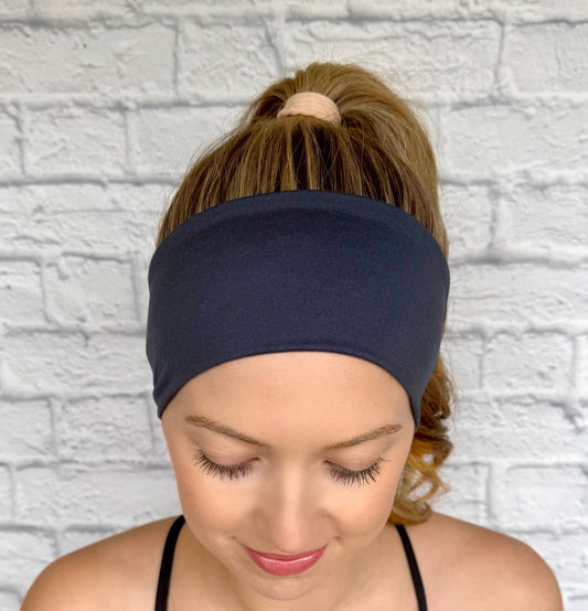 Woman with hair in ponytail wearing flat, stretchy headband in charcoal gray.