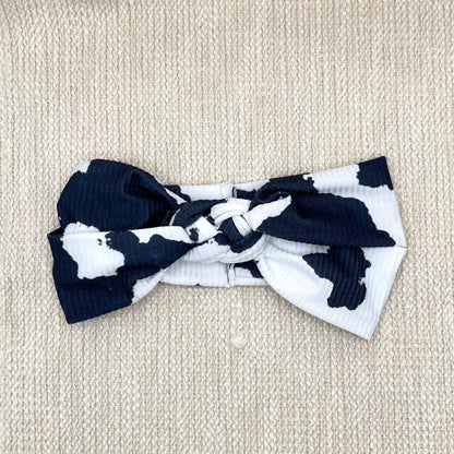 Black and white cow print headband in sailor knot style with ribbed fabric.