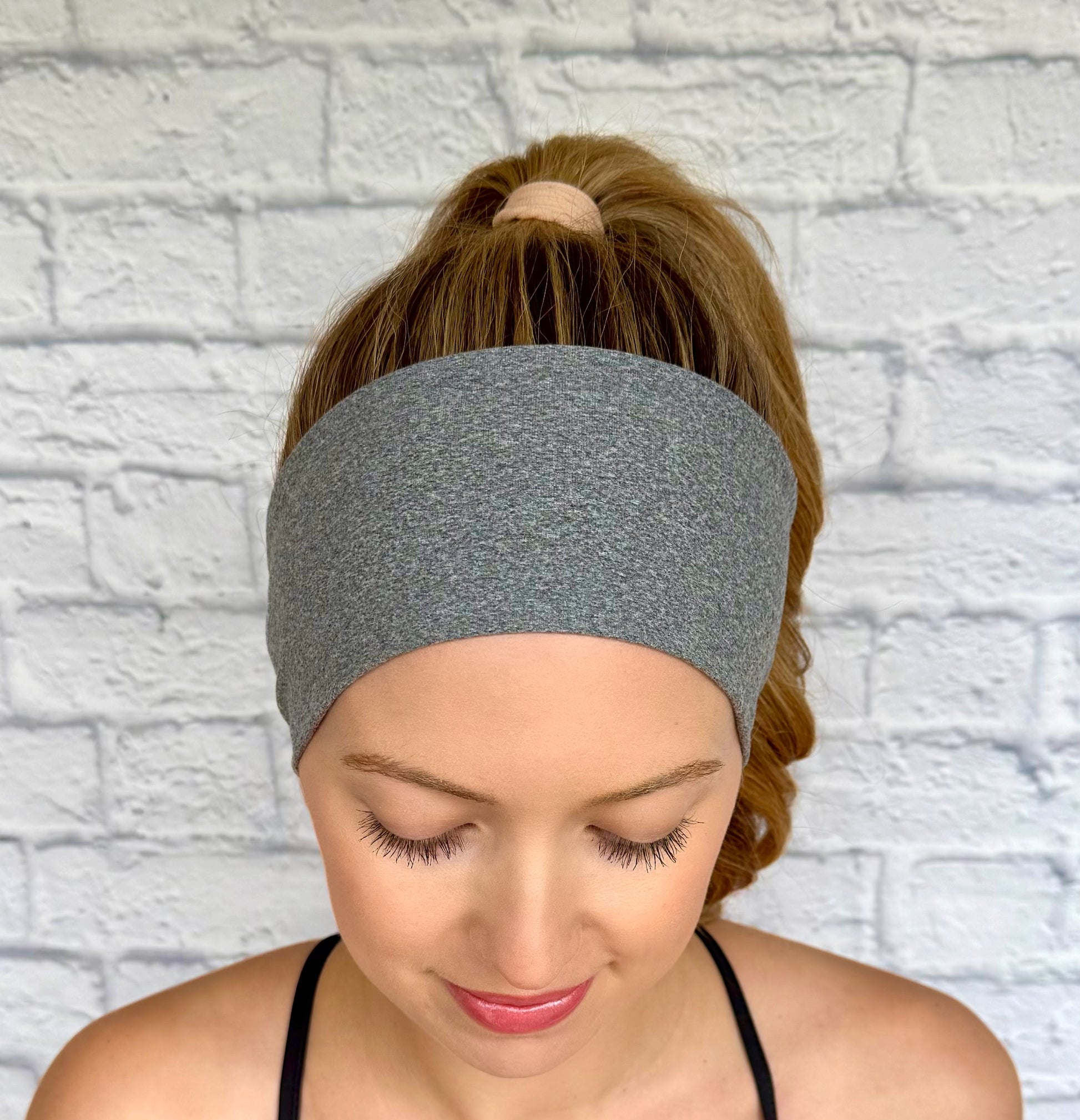 Woman with curled hair in ponytail wearing flat, stretchy, heather gray headband.