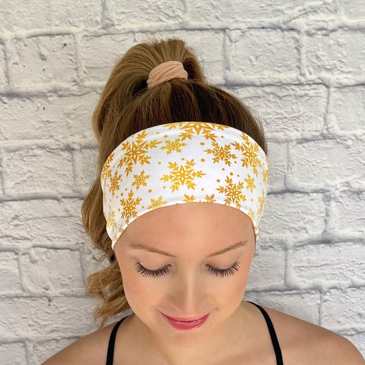 Woman with hair in curled ponytail wearing white, flat, stretchy headband with gold snowflake print.