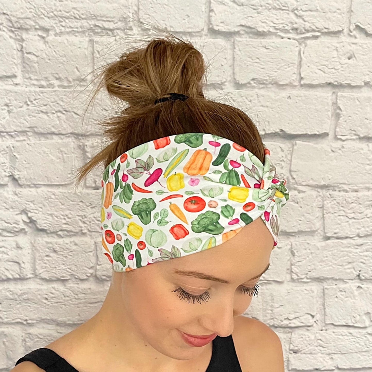 Woman with hair in bun wearing wide, twisted headband in white with vegetable theme print.