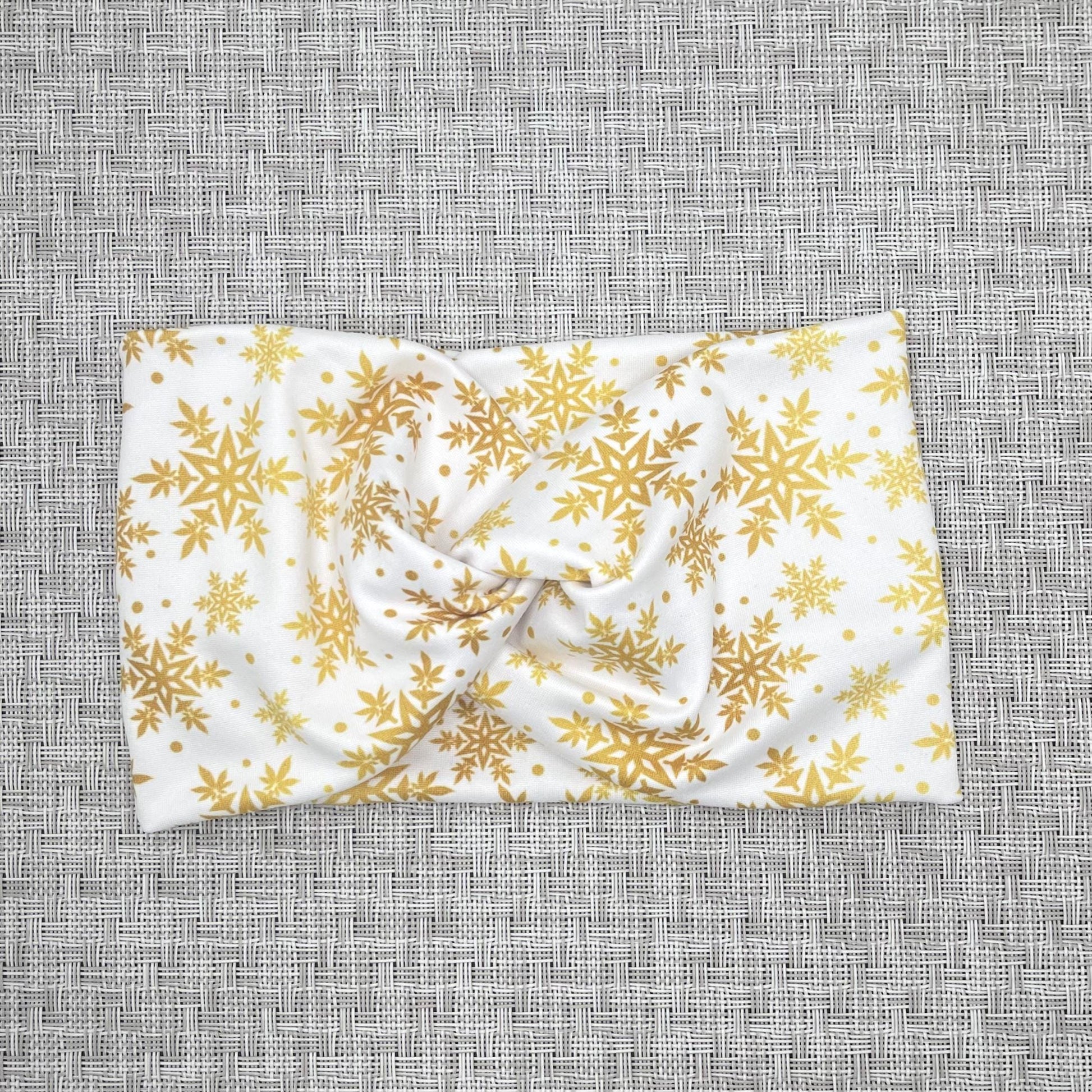 Wide, white, twisted headband with gold color snowflake print on gray background.