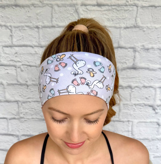 Woman with hair in ponytail wearing flat, stretchy, light gray headband with stork and baby theme print.