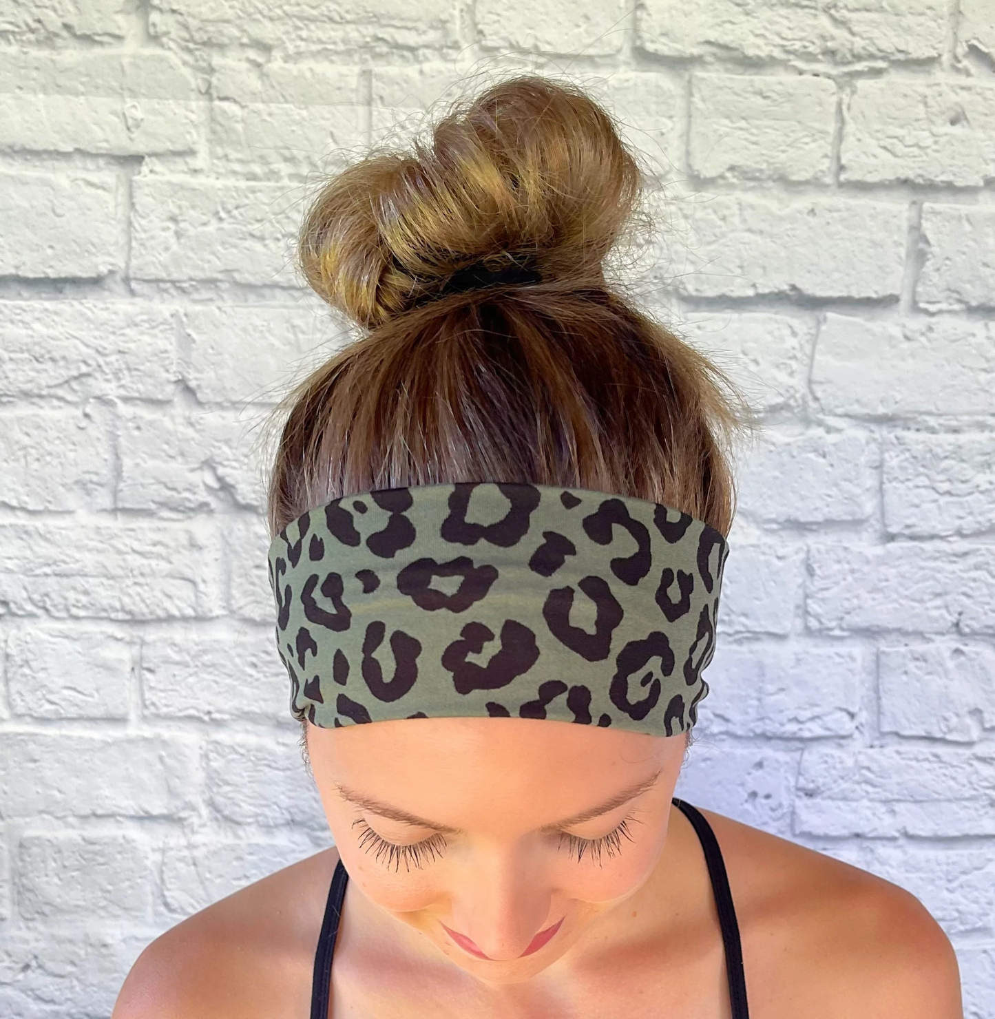 Woman with hair in bun wearing stretchy, green headband with black cheetah print.