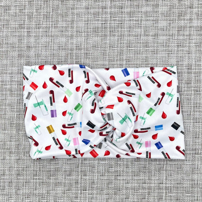 white, wide twist headband with phlebotomy theme print- blood vials, blood drops, and syringes