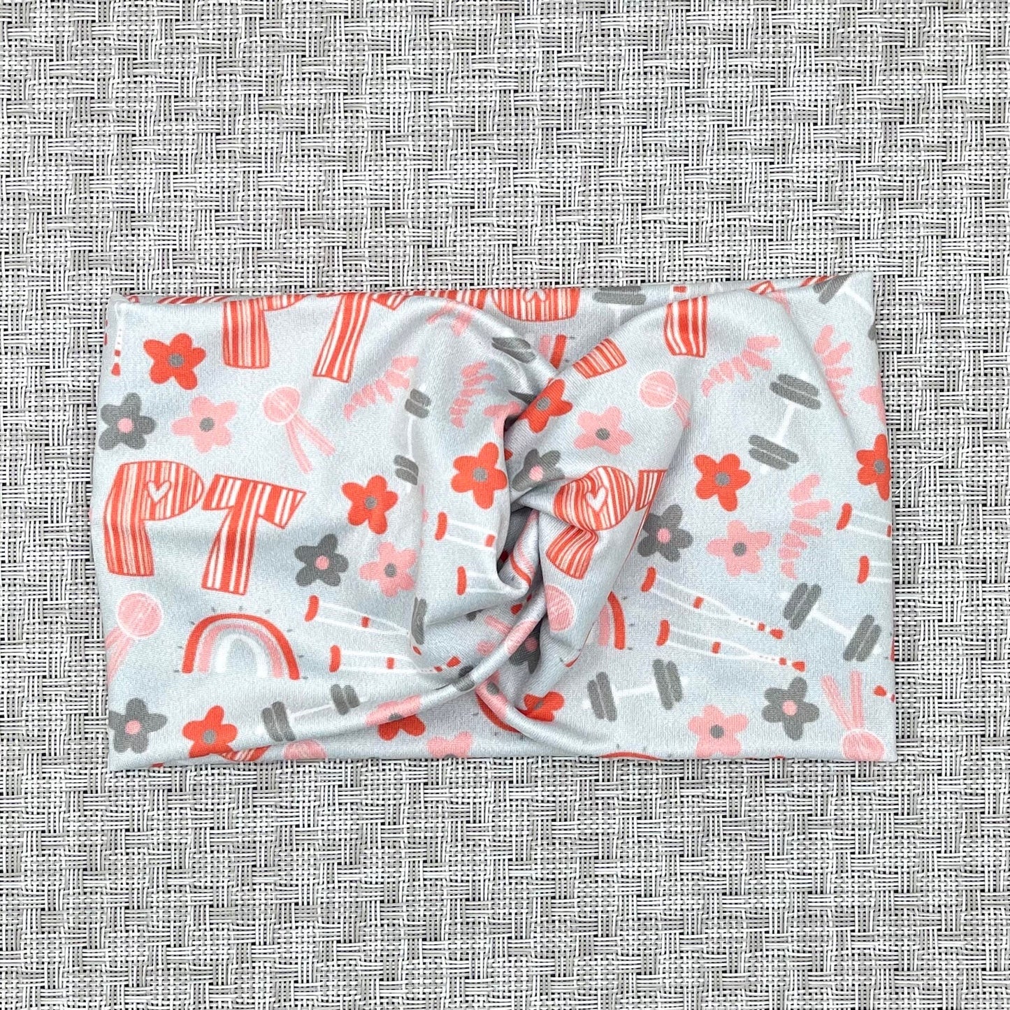 light blue/gray wide twist headband with "PT" print in orange and PT theme print with flowers in dark gray/blue and orange