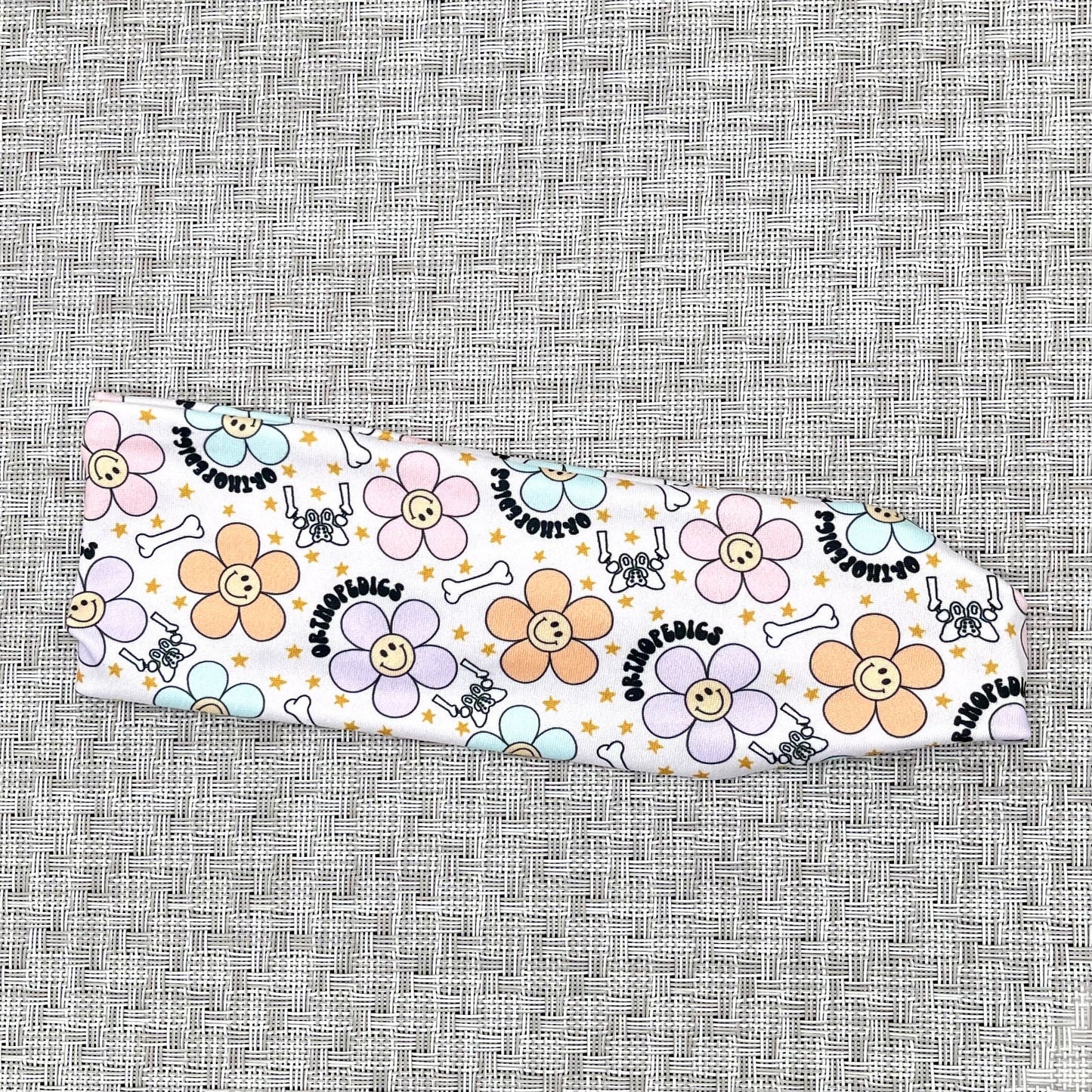 cream headband with "orthopedics" print, flowers with smiley faces, stars, and bones