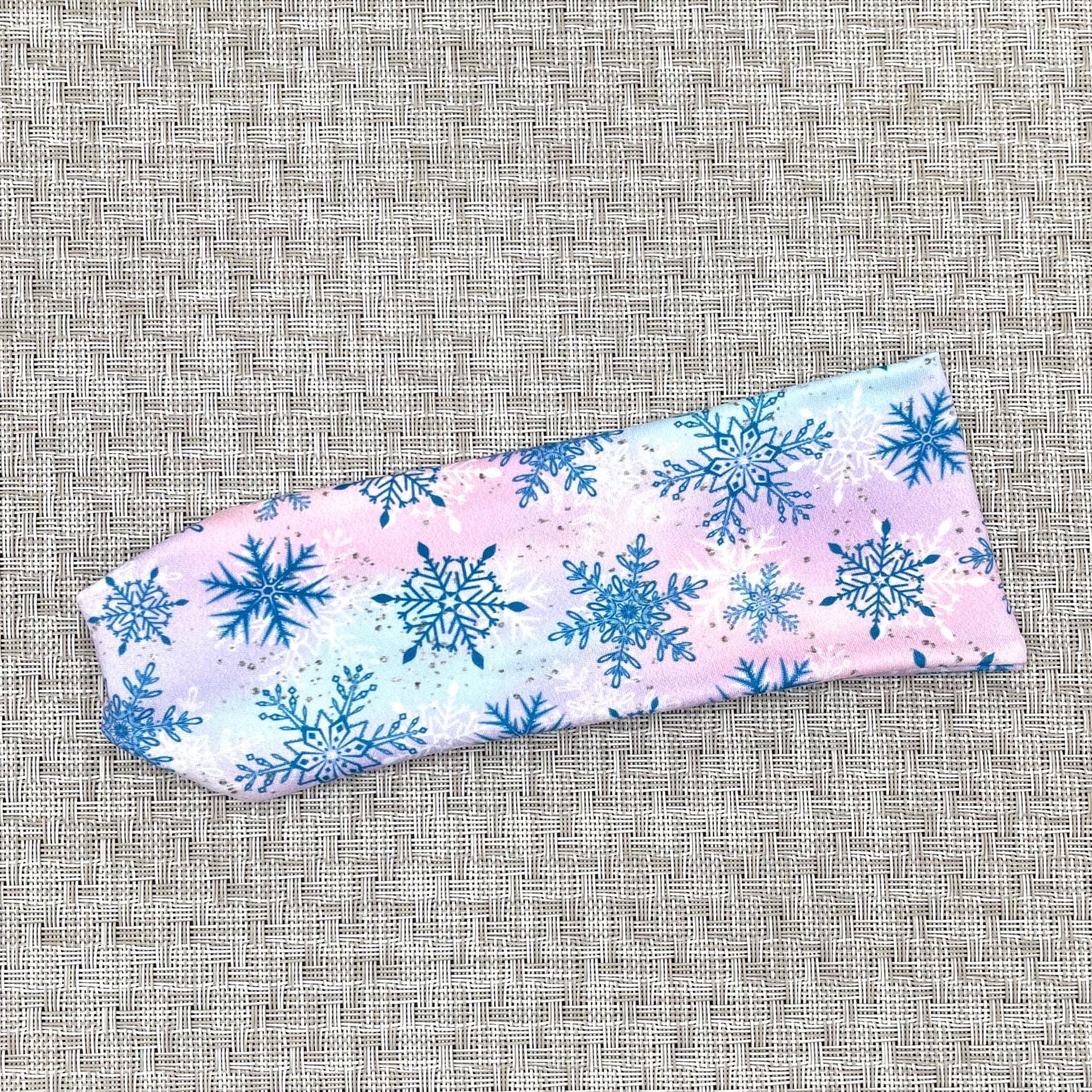 Stretchy, flat headband with purple and blue background with darker blue and white snowflake print.