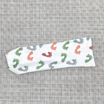 White headband with baby feet print in colors peach, wine, green, and light blue.