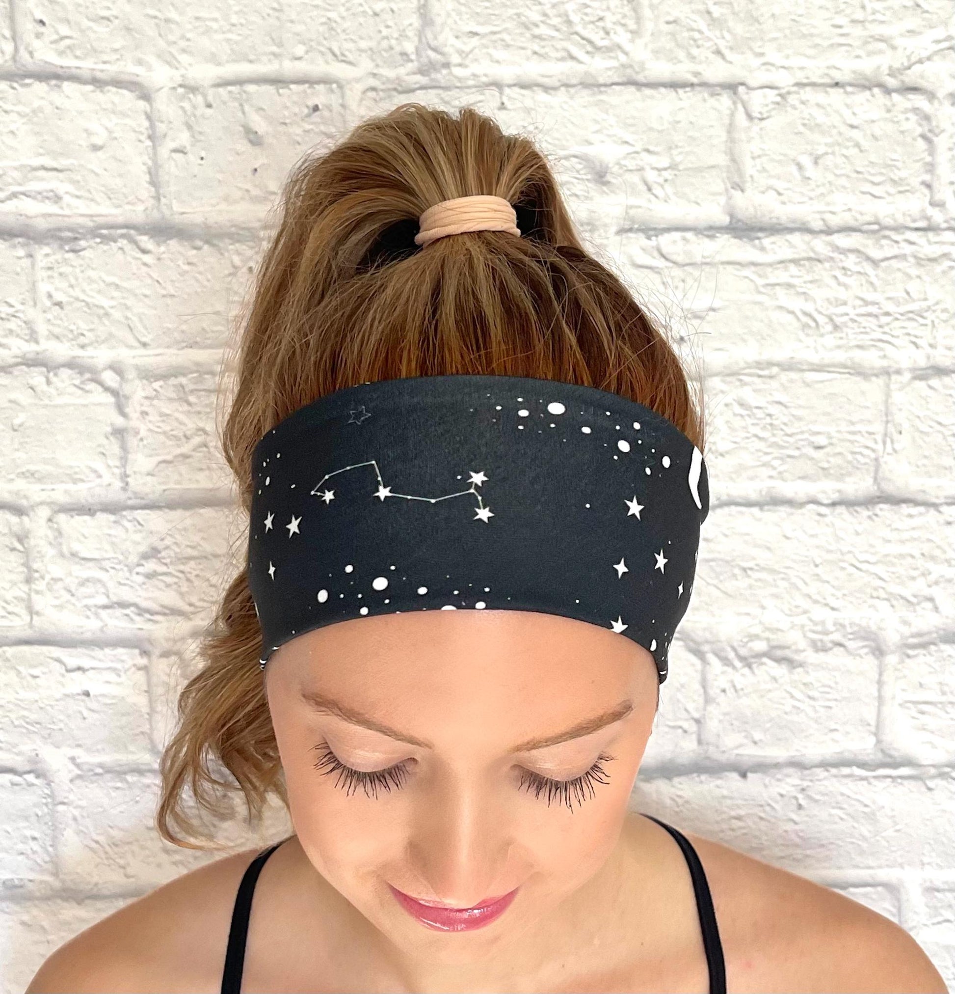 Woman with hair in ponytail wearing black headband with white space/galaxy theme print.