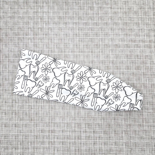 White, stretchy headband on gray background with black dental and floral theme print.