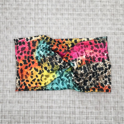 Wide, twisted headband with rainbow color cheetah print on a gray background.