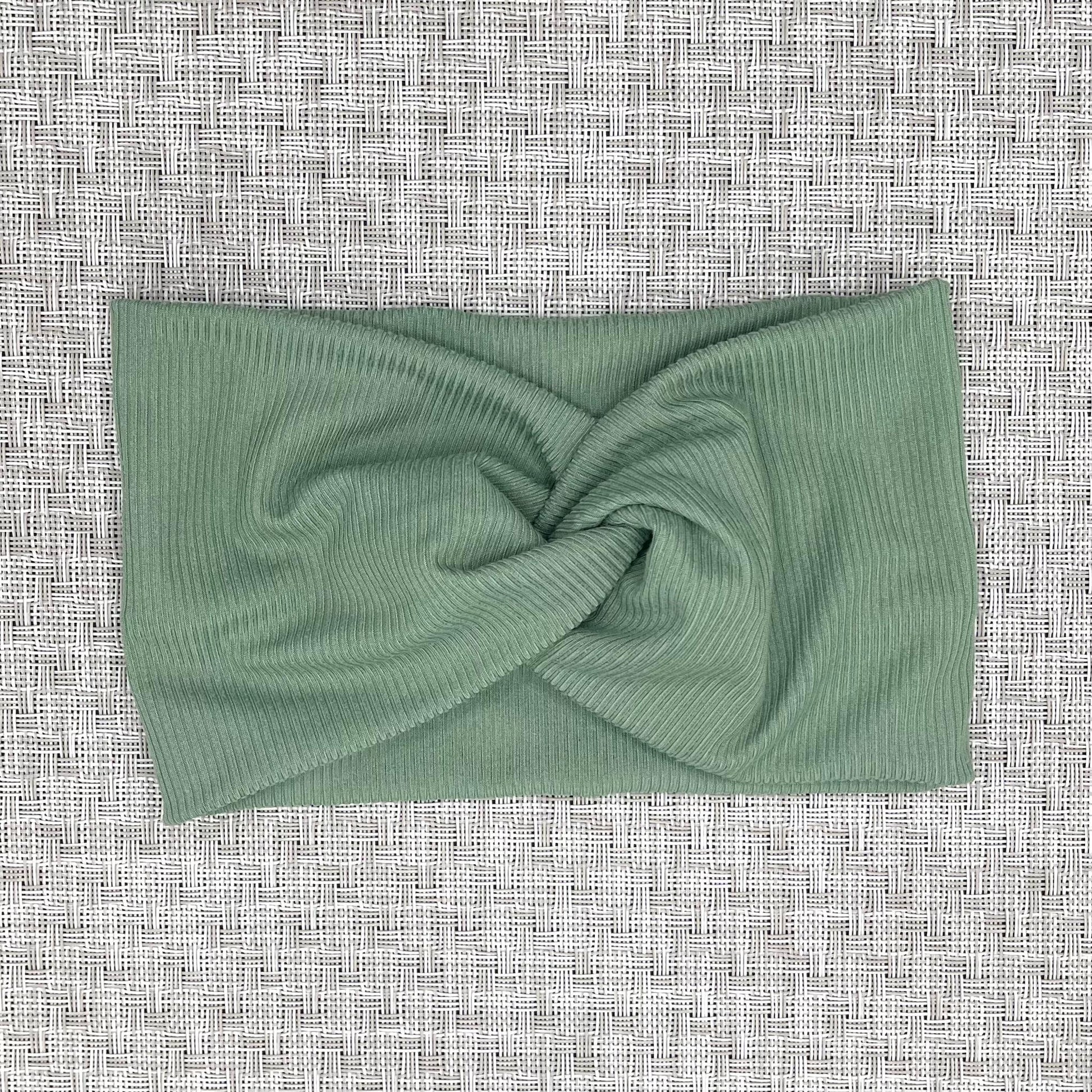 Wide, twisted headband with sage green ribbed fabric on a gray background.