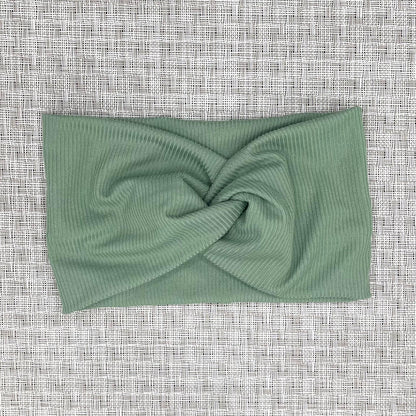 Wide, twisted headband with sage green ribbed fabric on a gray background.