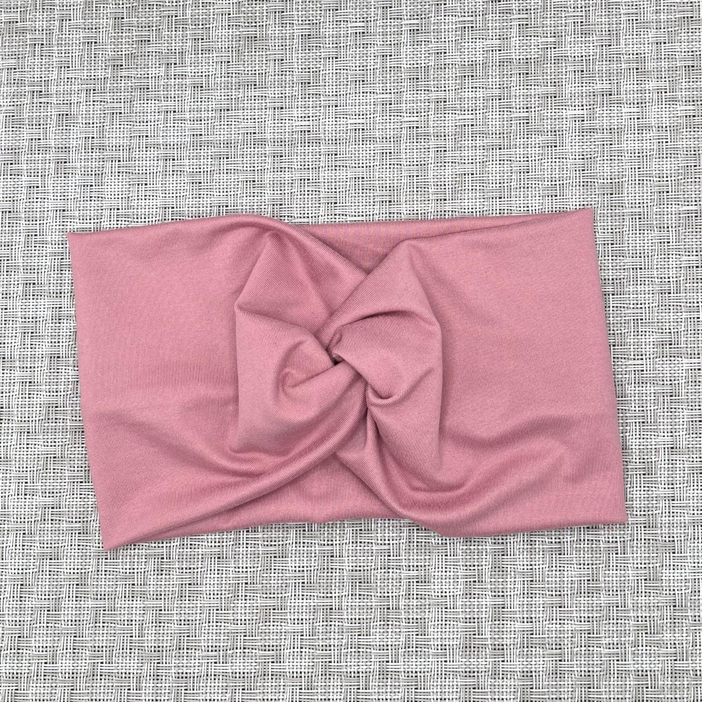 Wide, twisted headband in pink color on gray background.