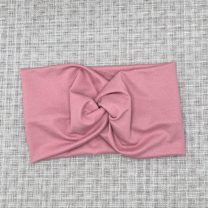 Wide, twisted headband in pink color on gray background.