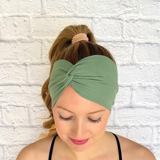 Woman with hair in curled ponytail wearing wide, twisted headband with sage green ribbed fabric.