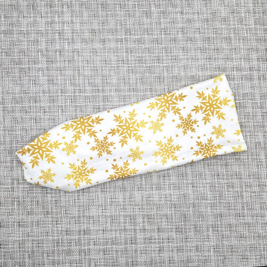 White, flat, stretchy headband with gold snowflake print on gray background.