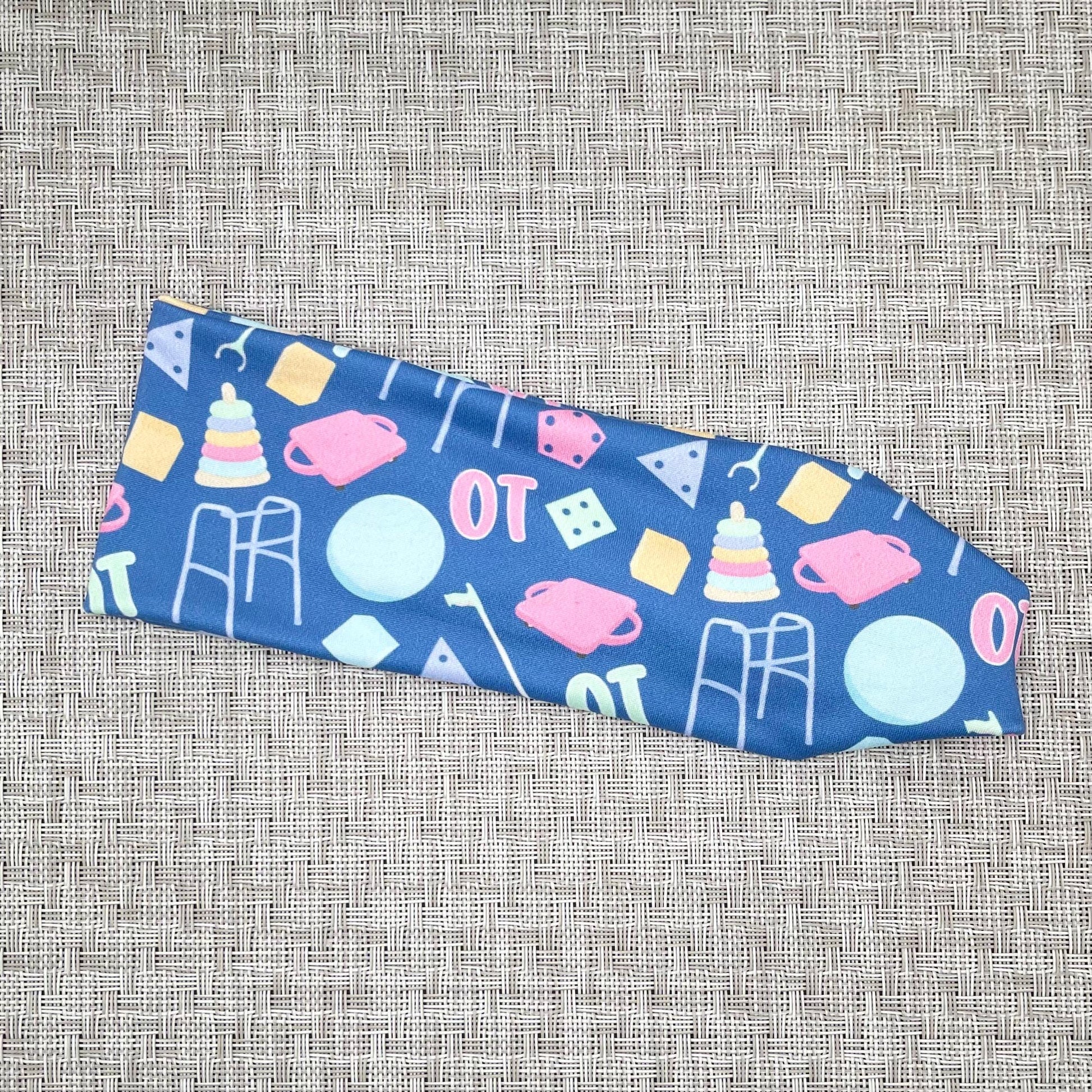 Flat, stretchy, blue headband with "OT" and occupational therapy accessories theme print.