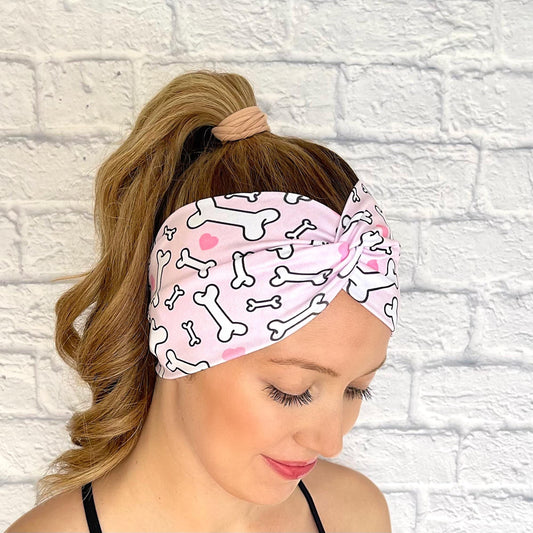Woman with hair in curled ponytail wearing wide, twisted headband in light pink with dog bone and heart print.