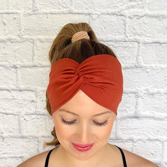 Woman with hair in curled ponytail wearing wide, twisted headband in burnt orange color.