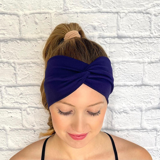 Woman with hair in curled ponytail wearing wide, twisted headband in dark blue/navy color.