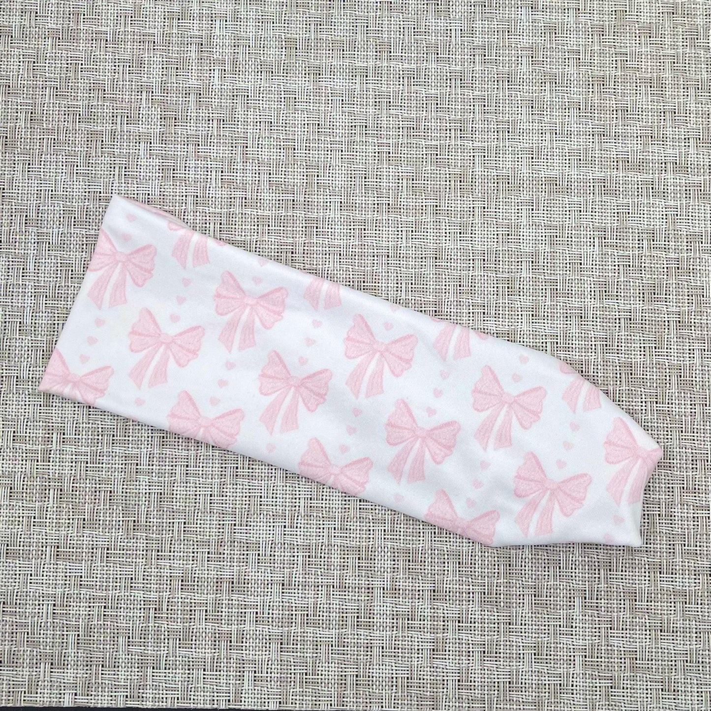 Flat, stretchy, white headband with light pink bow print on a gray background.