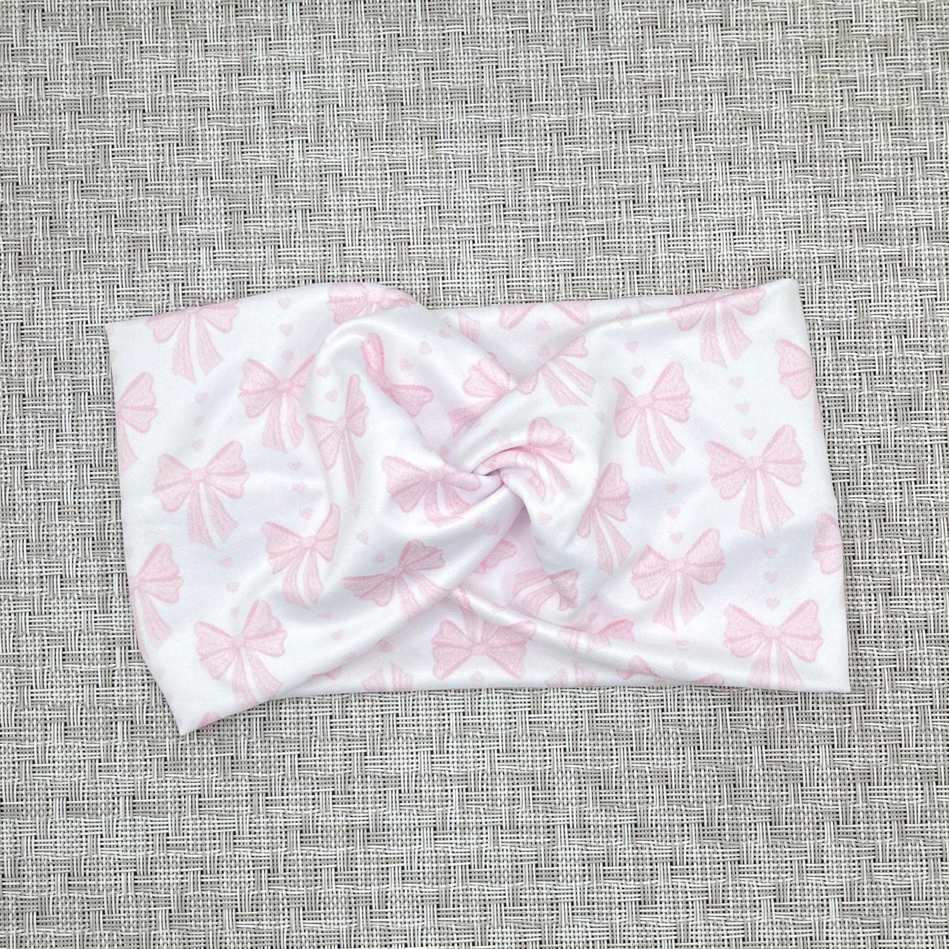 Wide, twisted headband in white with light pink bow print on gray background.