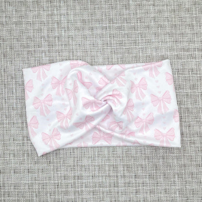 Wide, twisted headband in white with light pink bow print on gray background.