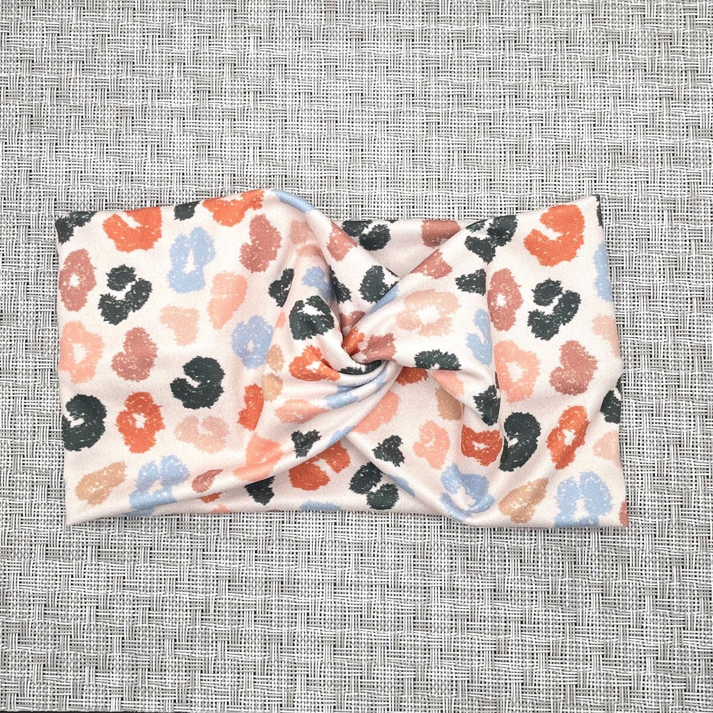 Wide, twisted headband in cream color with cheetah print in varying shades of blues, orange/peach, and tan.