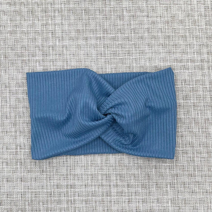 Wide, twisted, stretchy headband in blue ribbed fabric.