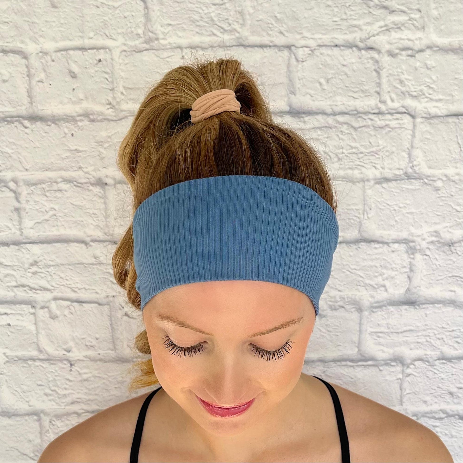 Woman with hair in curled ponytail wearing flat, stretchy headband in blue ribbed fabric.