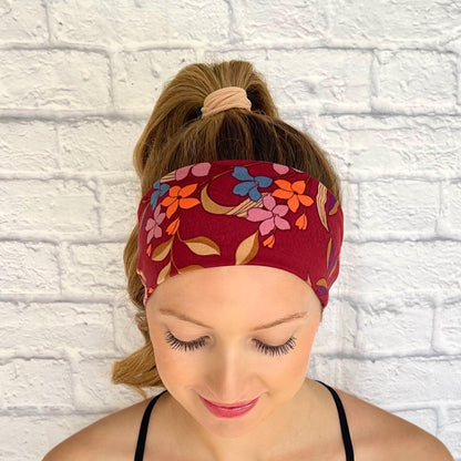 Woman with hair in curled ponytail wearing flat, stretchy headband in maroon with floral print.