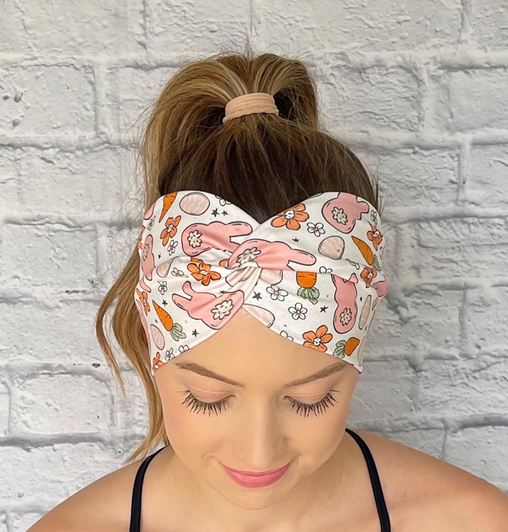 Woman with hair in curled ponytail wearing wide, twisted headband in white with orange and peach Easter theme print.