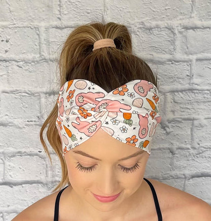 Woman with hair in curled ponytail wearing wide, twisted headband in white with orange and peach Easter theme print.