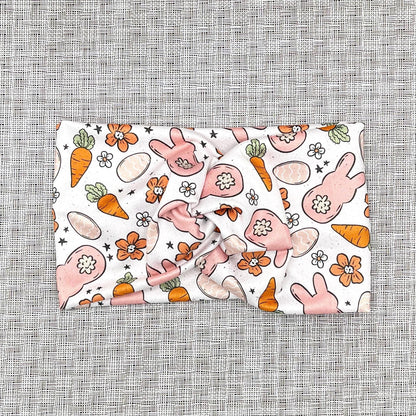 Wide, twisted headband in white with orange and peach Easter theme print.
