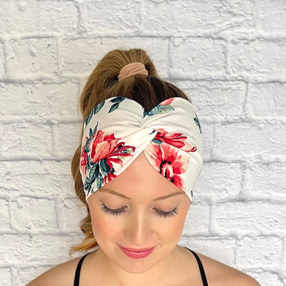 Woman with hair in curled ponytail wearing wide, twisted headband in white with red/pink rose print.