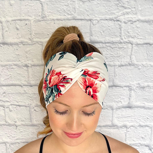 Woman with hair in curled ponytail wearing wide, twisted headband in white with red/pink rose print.